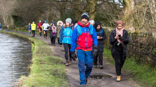 A group of people in waterproof coats and woolly hats, walking on a path beside a waterway.